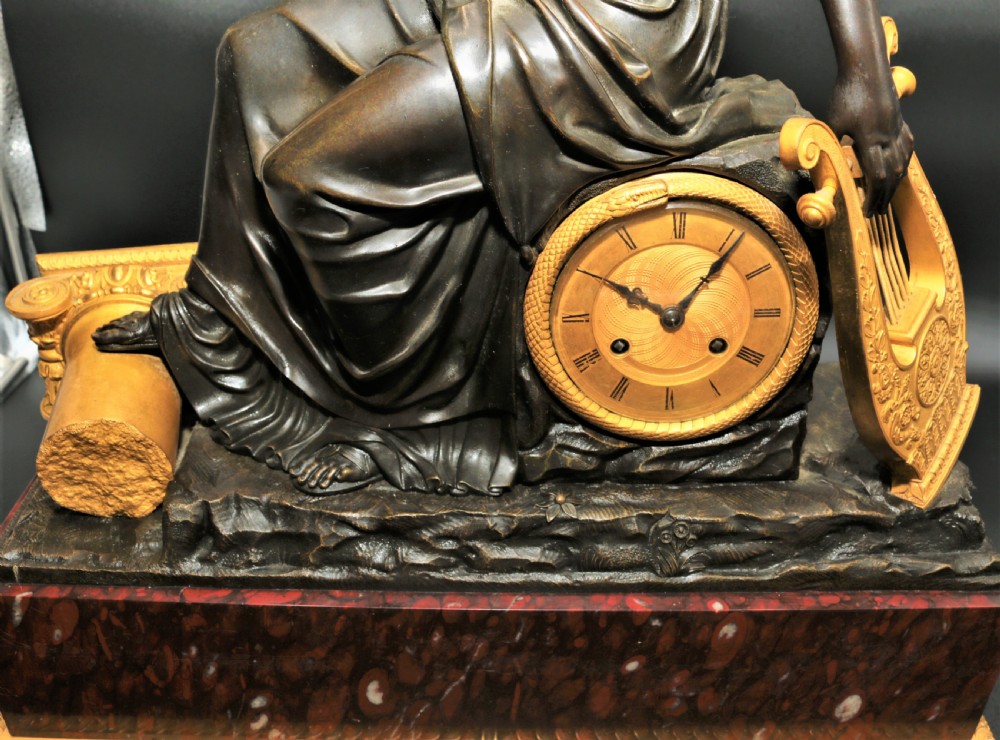A French Empire mantel clock featuring a dark patinated bronze classical female figure holding a lyre, positioned beside a gold-coloured dial on a red marble base with gilt metal mounts. View XIII