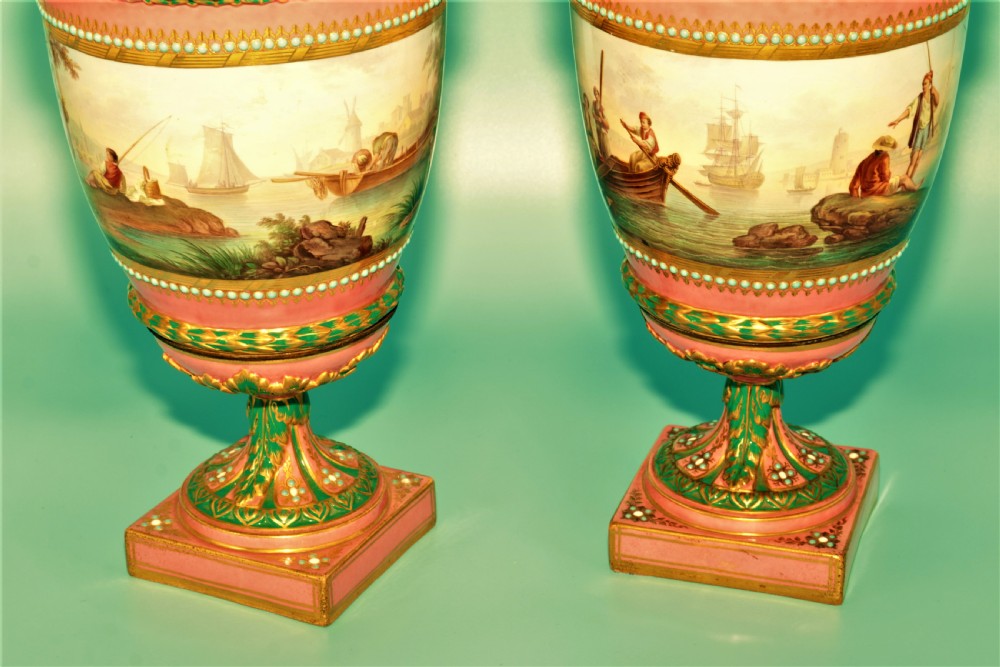 A pair of hand-painted pink porcelain urns featuring romantic pastoral figures, green detailing, intricate gilding, and square pedestal bases. View V