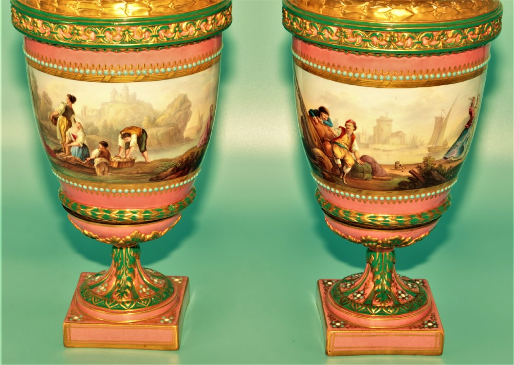 A pair of hand-painted pink porcelain urns featuring romantic pastoral figures, green detailing, intricate gilding, and square pedestal bases. View VI