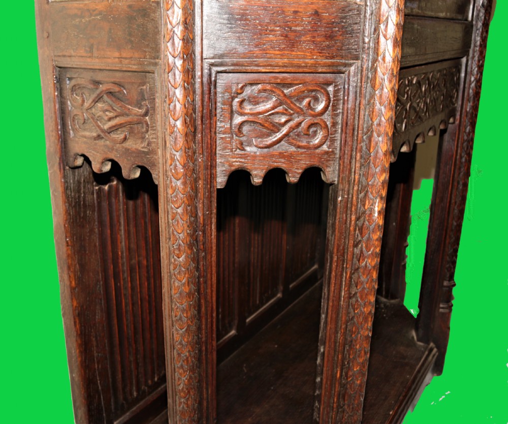 A dark carved oak Gothic Revival display cabinet featuring a glazed upper section, patterned fabric lining, and detailed linenfold panelling on the lower frame. View VIII