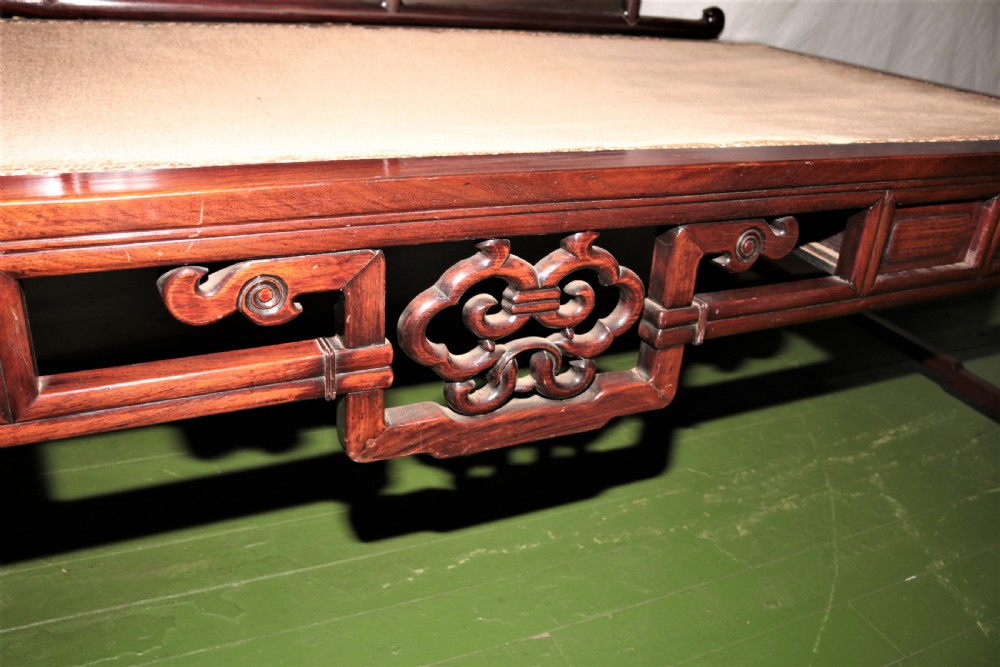 A carved dark hardwood Chinese daybed featuring a stepped backrest with marble panel inserts and a tufted light brown cushioned seat. View VI
