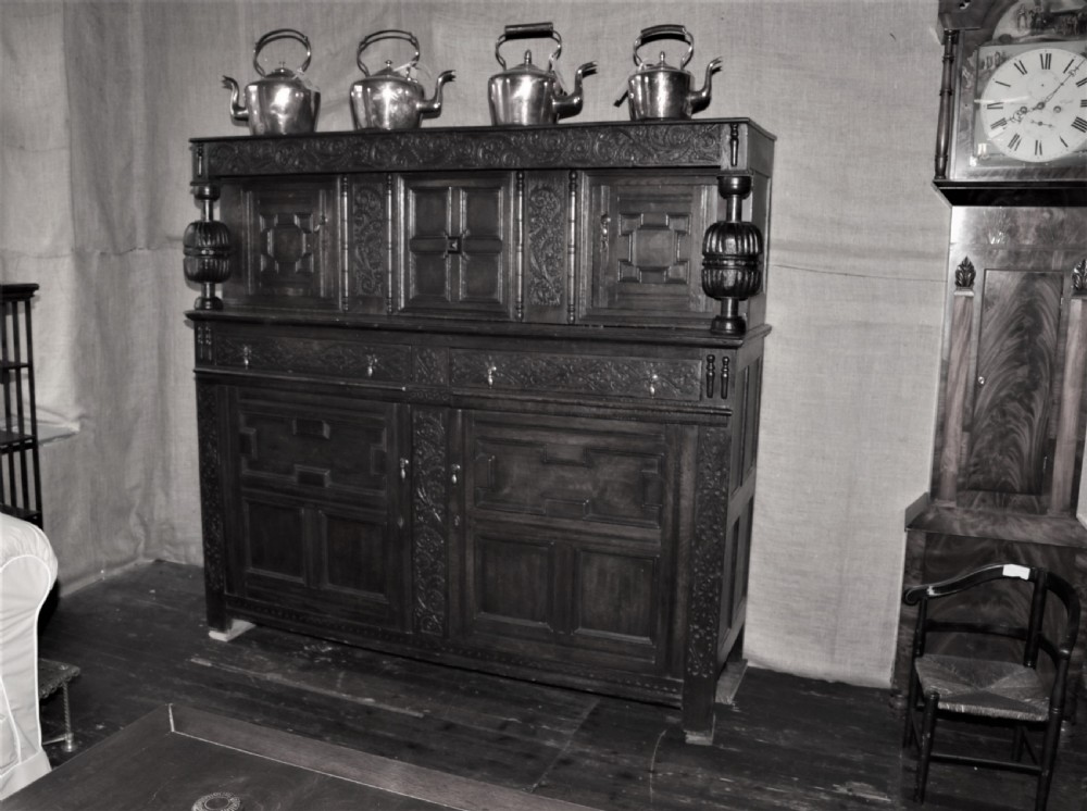 A dark carved oak Elizabethan court cupboard featuring geometric panelled doors, bulbous turned supports, and intricate foliate carvings. View II