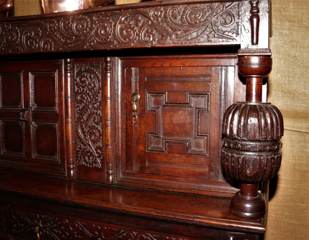 A dark carved oak Elizabethan court cupboard featuring geometric panelled doors, bulbous turned supports, and intricate foliate carvings. View III