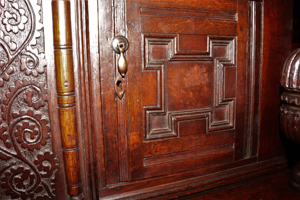 A dark carved oak Elizabethan court cupboard featuring geometric panelled doors, bulbous turned supports, and intricate foliate carvings. View IV