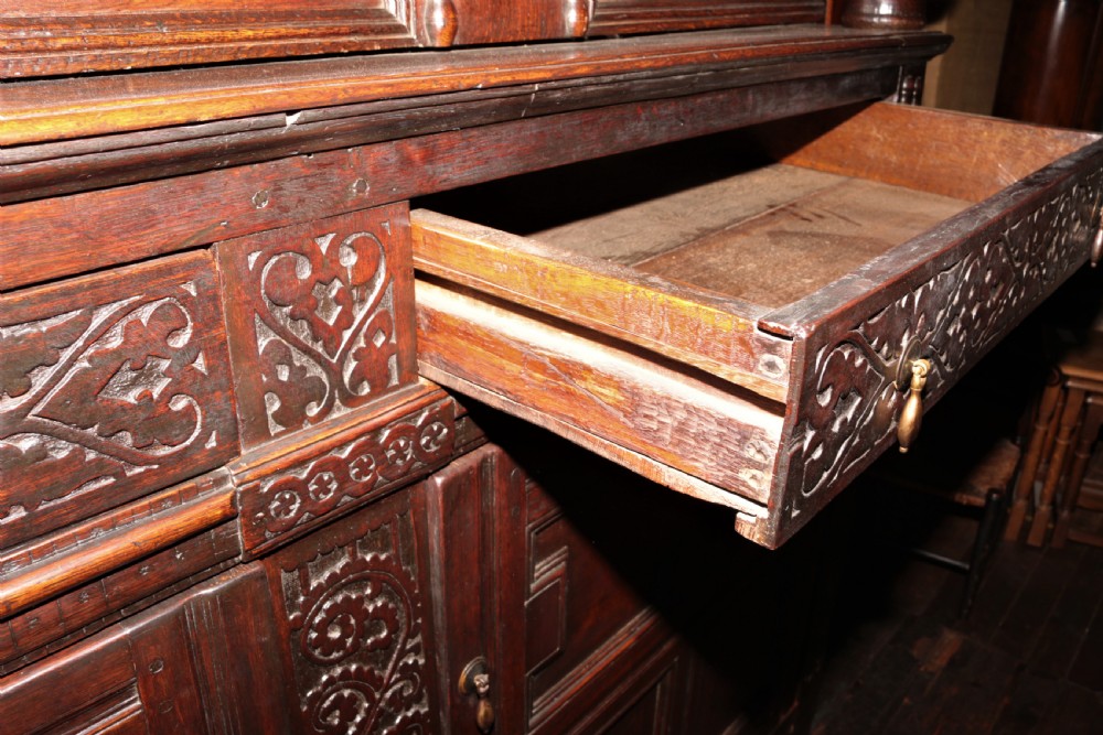 A dark carved oak Elizabethan court cupboard featuring geometric panelled doors, bulbous turned supports, and intricate foliate carvings. View VI