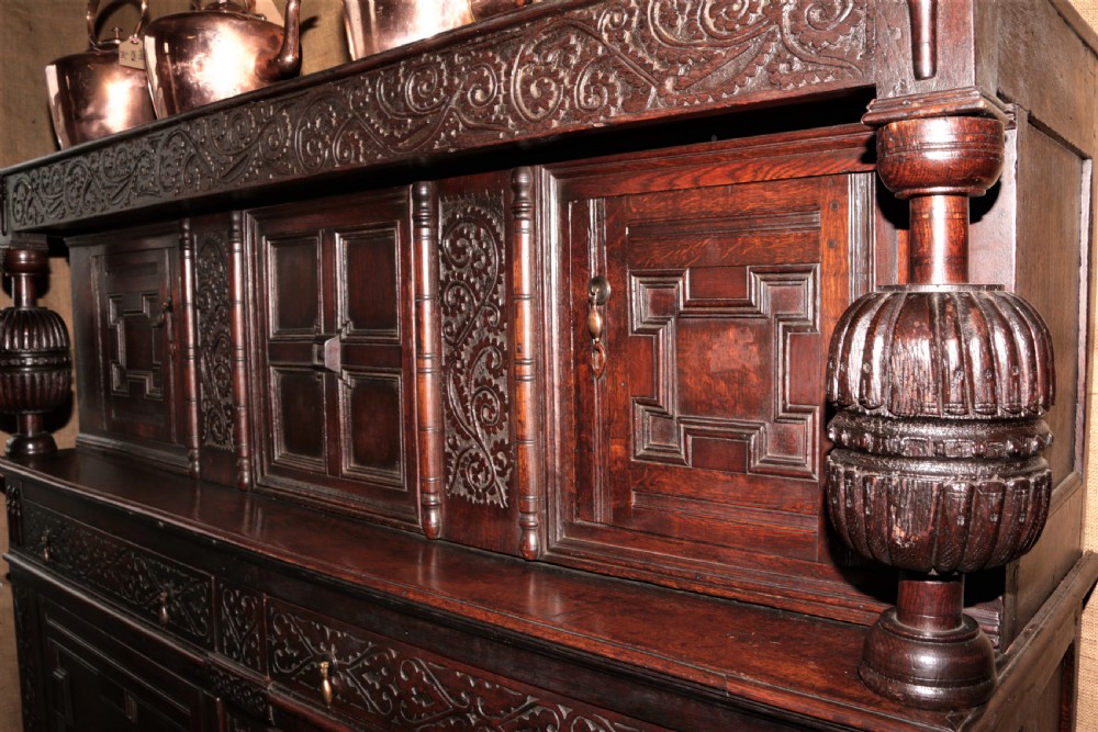 A dark carved oak Elizabethan court cupboard featuring geometric panelled doors, bulbous turned supports, and intricate foliate carvings. View XI