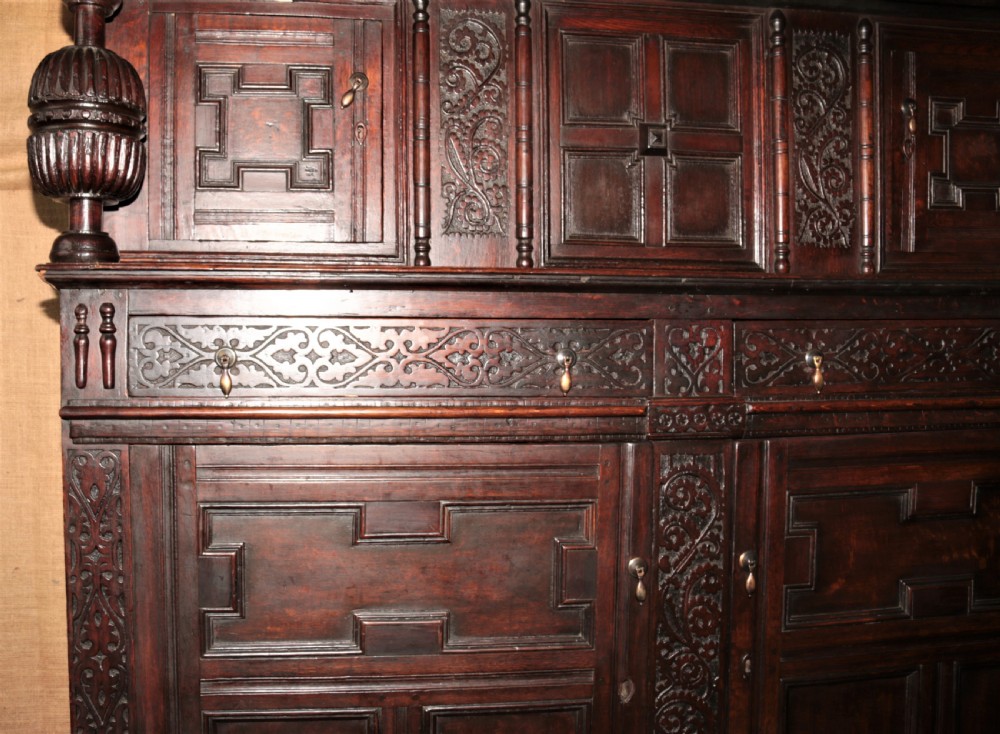 A dark carved oak Elizabethan court cupboard featuring geometric panelled doors, bulbous turned supports, and intricate foliate carvings. View XVI