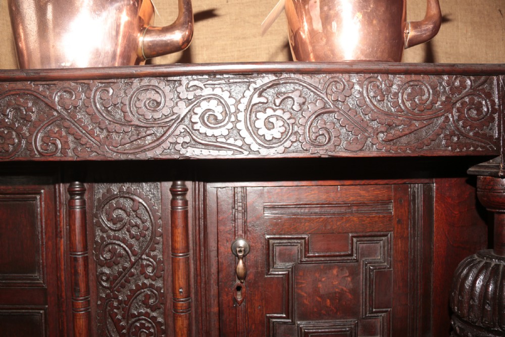 A dark carved oak Elizabethan court cupboard featuring geometric panelled doors, bulbous turned supports, and intricate foliate carvings. View XVIII