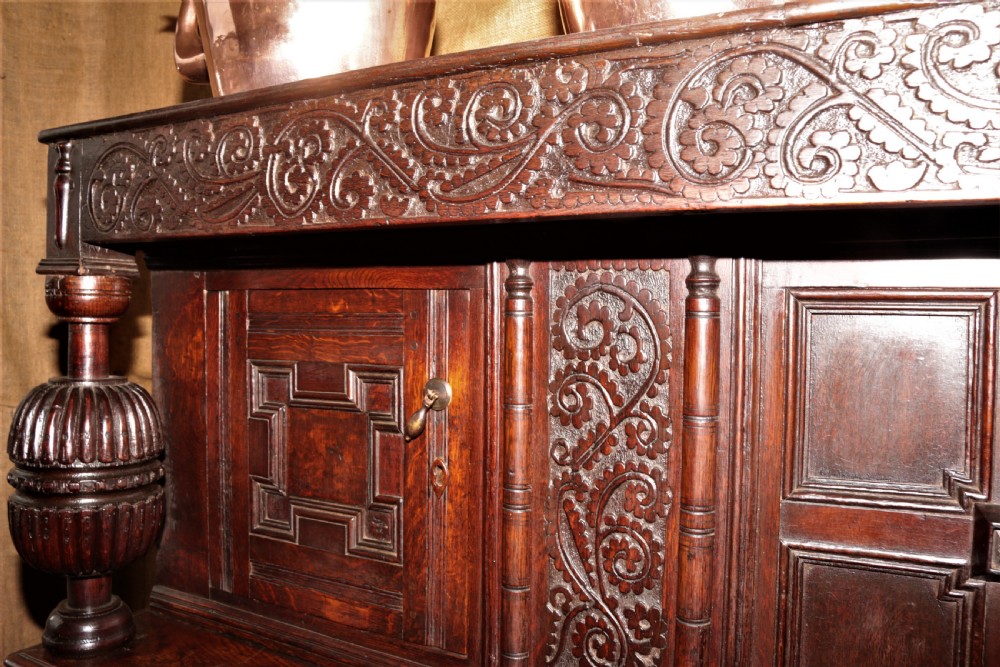 A dark carved oak Elizabethan court cupboard featuring geometric panelled doors, bulbous turned supports, and intricate foliate carvings. View XIX