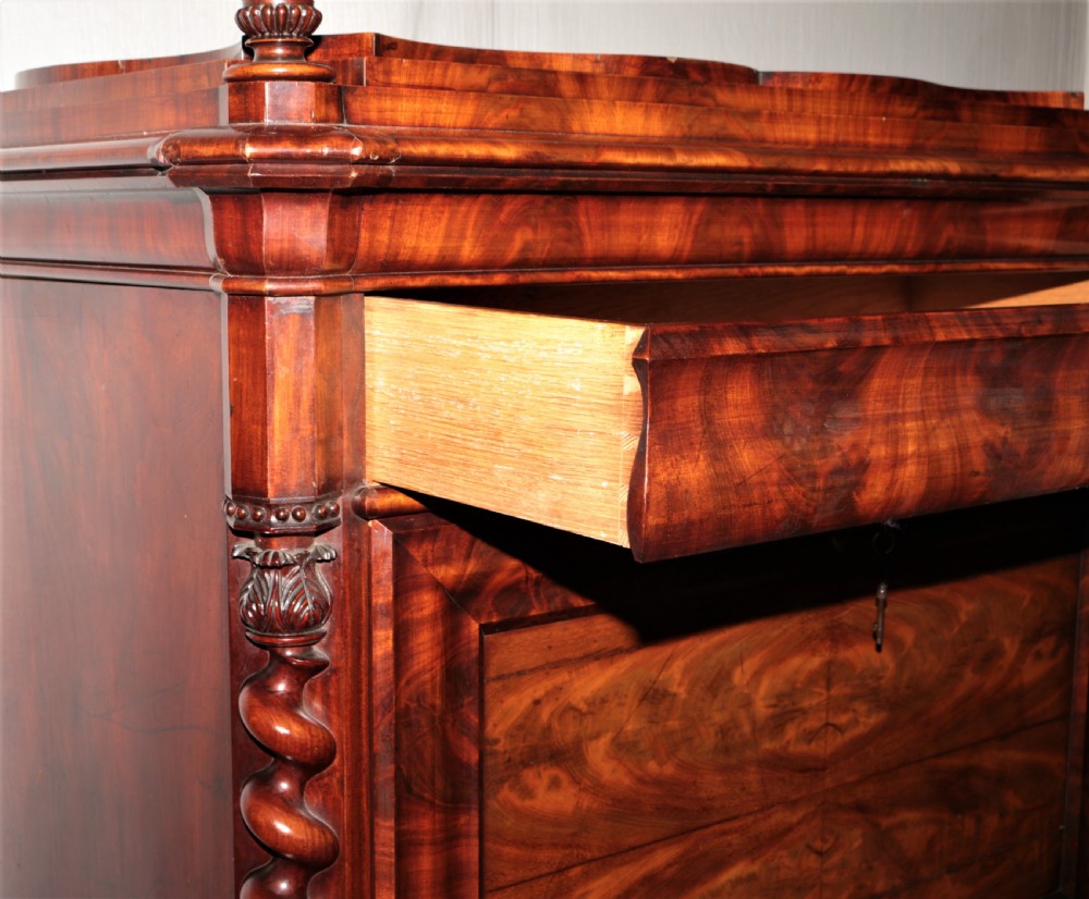 A Biedermeier flame mahogany fall-front bureau desk featuring twisted side columns, multiple drawers, brass keyhole escutcheons, and urn finials. View V