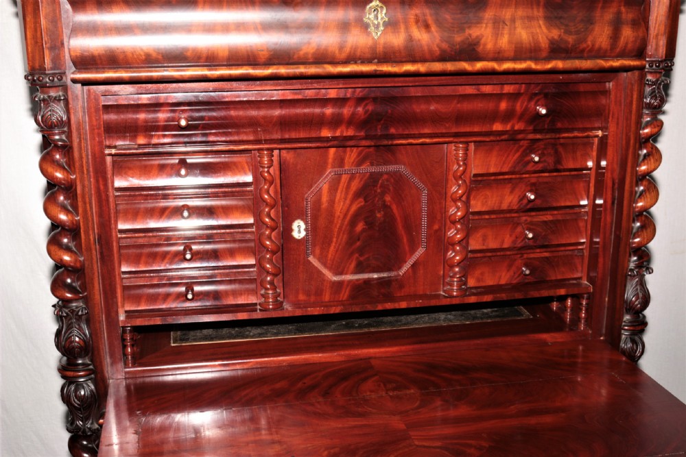 A Biedermeier flame mahogany fall-front bureau desk featuring twisted side columns, multiple drawers, brass keyhole escutcheons, and urn finials. View VIII