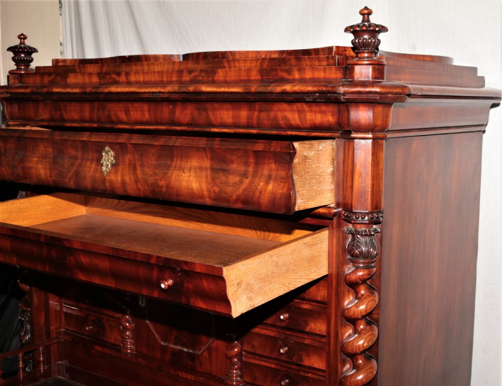 A Biedermeier flame mahogany fall-front bureau desk featuring twisted side columns, multiple drawers, brass keyhole escutcheons, and urn finials. View XI
