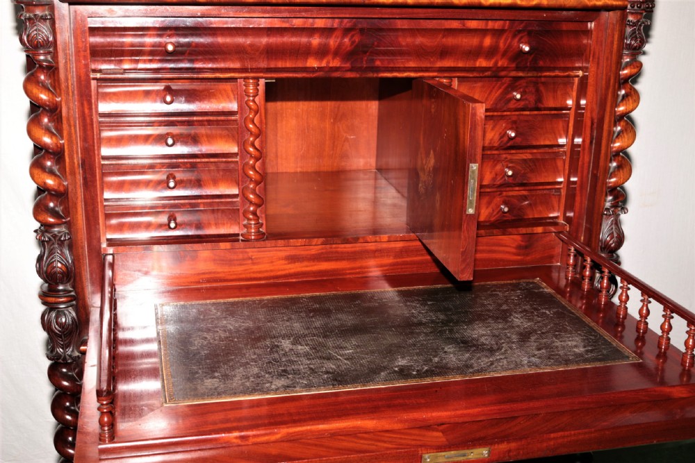 A Biedermeier flame mahogany fall-front bureau desk featuring twisted side columns, multiple drawers, brass keyhole escutcheons, and urn finials. View XII