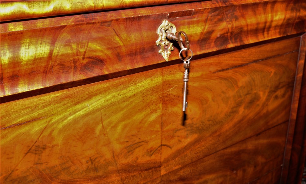 A Biedermeier flame mahogany fall-front bureau desk featuring twisted side columns, multiple drawers, brass keyhole escutcheons, and urn finials. View XIV