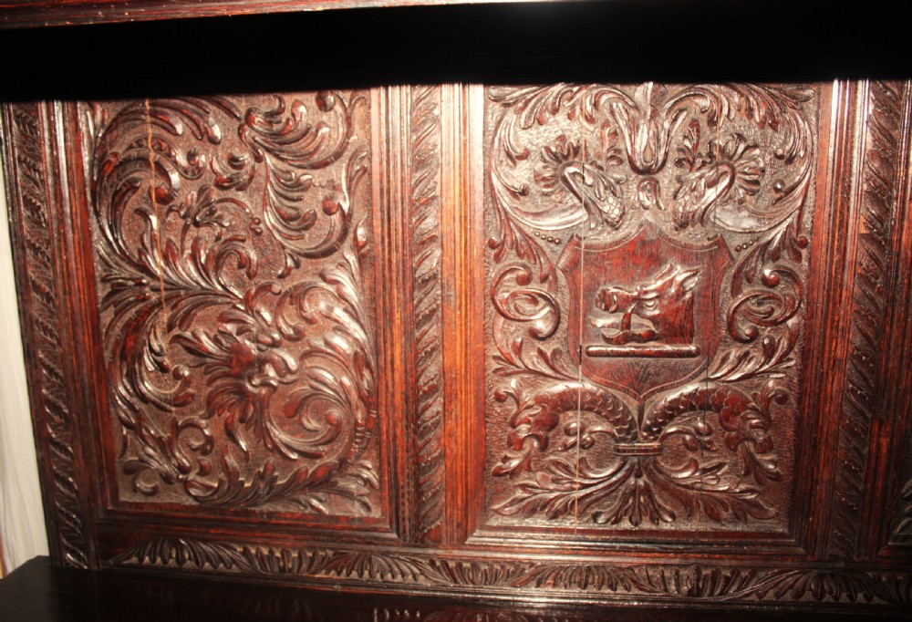 A dark carved oak dresser sideboard featuring intricate relief foliage panels, a central crest, upper shelving, and barley twist support columns. View II