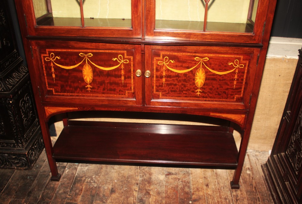 An Edwardian mahogany display cabinet featuring geometric astragal glazed doors, ribbon marquetry inlays, and an open lower undertier shelf. View II
