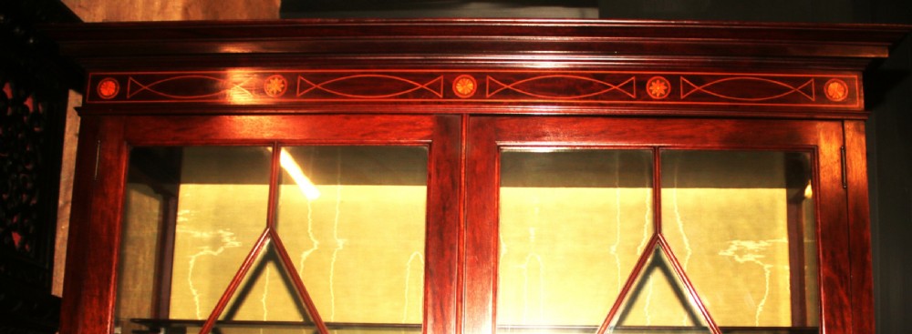An Edwardian mahogany display cabinet featuring geometric astragal glazed doors, ribbon marquetry inlays, and an open lower undertier shelf. View III