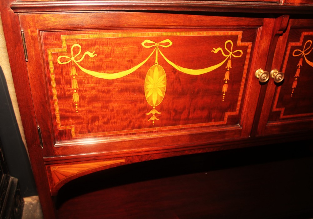 An Edwardian mahogany display cabinet featuring geometric astragal glazed doors, ribbon marquetry inlays, and an open lower undertier shelf. View VIII