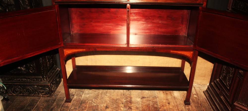 An Edwardian mahogany display cabinet featuring geometric astragal glazed doors, ribbon marquetry inlays, and an open lower undertier shelf. View IX