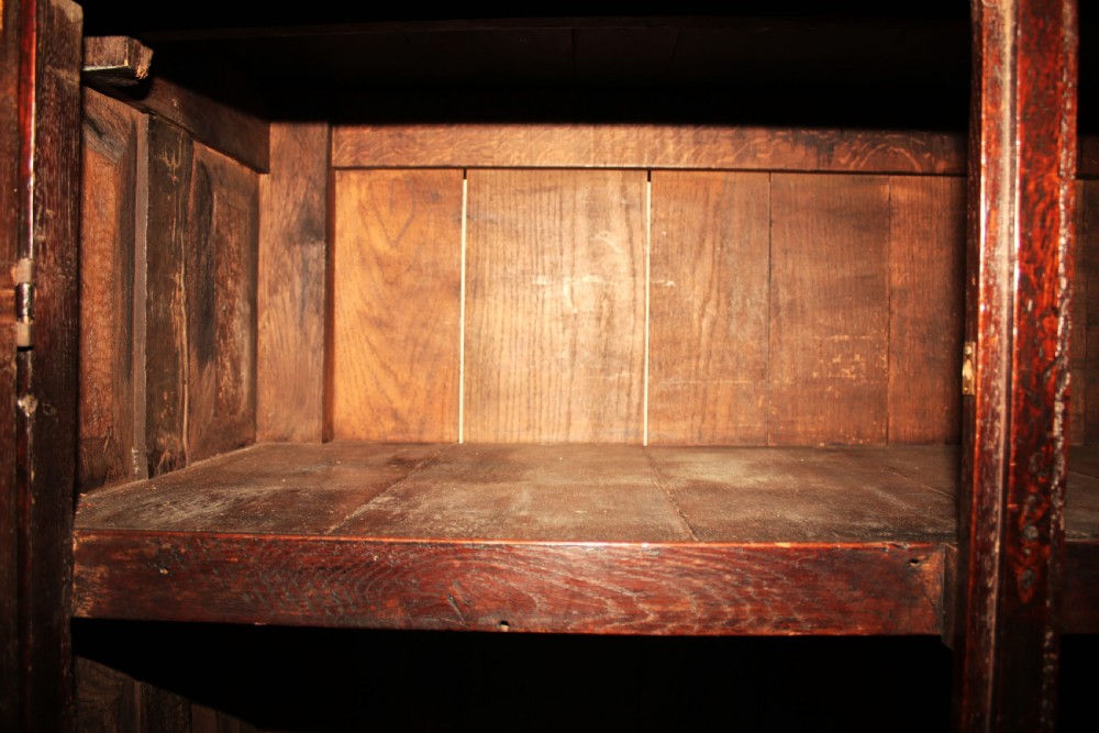 A dark oak court cupboard featuring a recessed upper section with carved panel doors and drop pendants above a lower two-door cabinet with iron hinges. View XIII