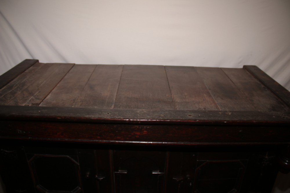 A dark oak court cupboard featuring a recessed upper section with carved panel doors and drop pendants above a lower two-door cabinet with iron hinges. View XIV