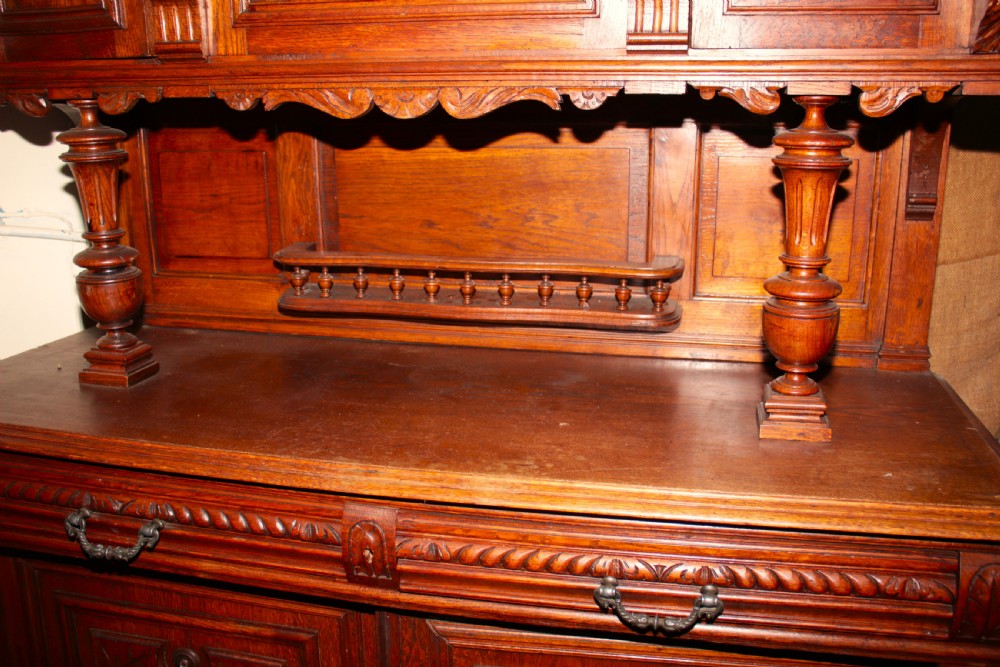 A large, two-tiered dark oak cabinet featuring intricate relief carvings, a central panel depicting a hunting scene, turned columns, and carved lower cupboards. View VIII