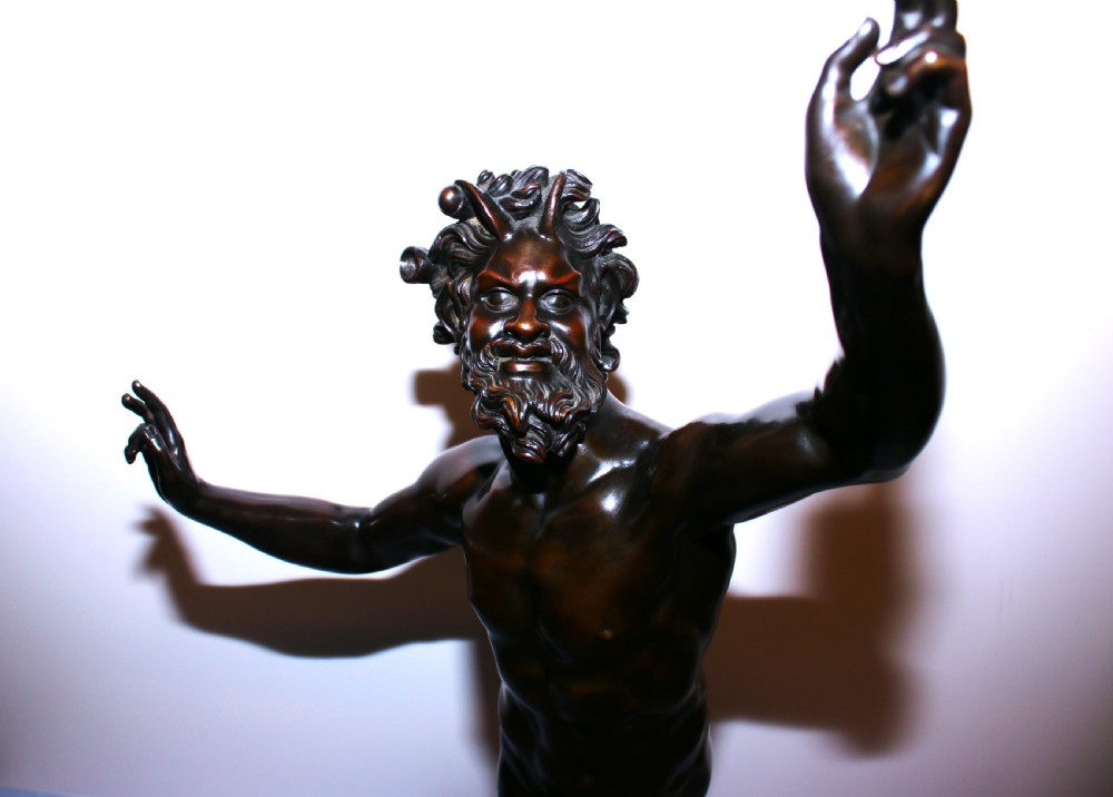 A dark patinated bronze sculpture of a dancing faun with raised arms mounted on a square marble base. View II