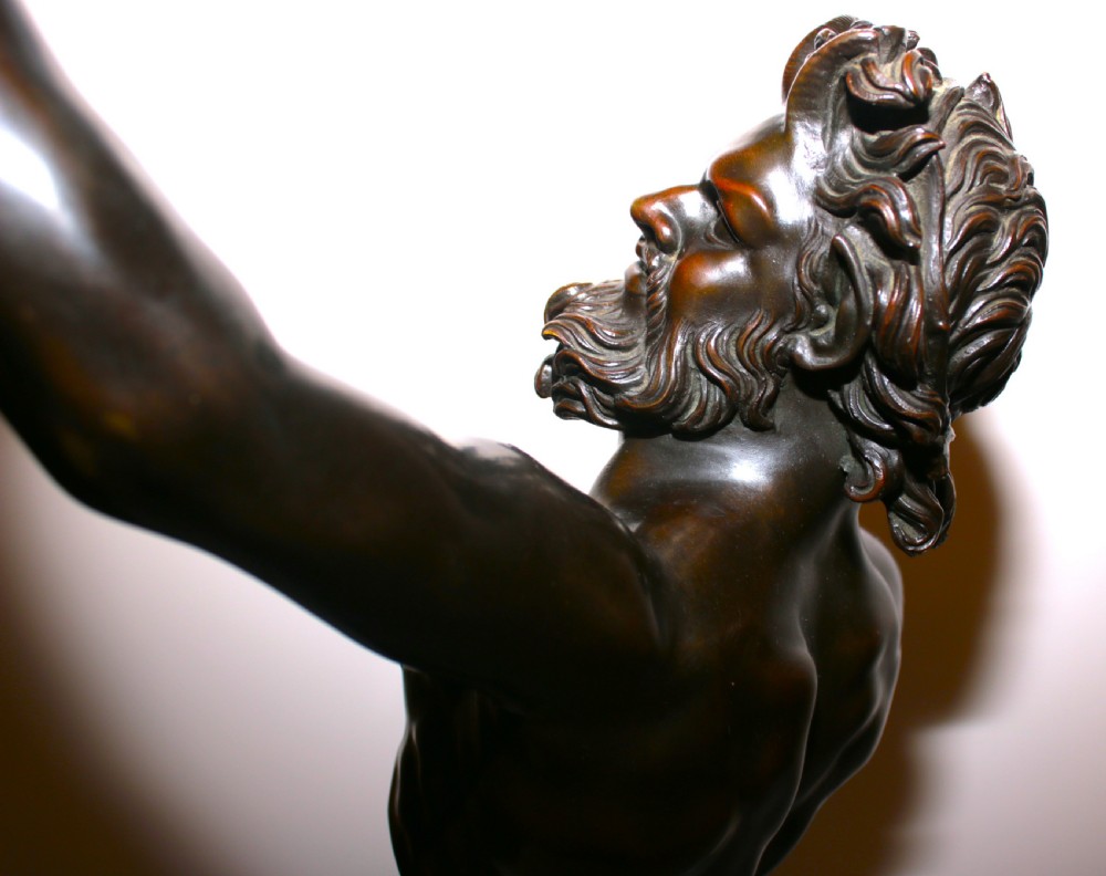 A dark patinated bronze sculpture of a dancing faun with raised arms mounted on a square marble base. View XV