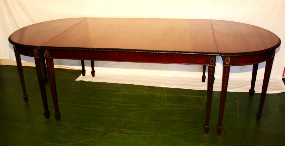 An antique dark mahogany extending dining table featuring removable leaves, D-shaped end sections, and tapered square legs with carved detailing.