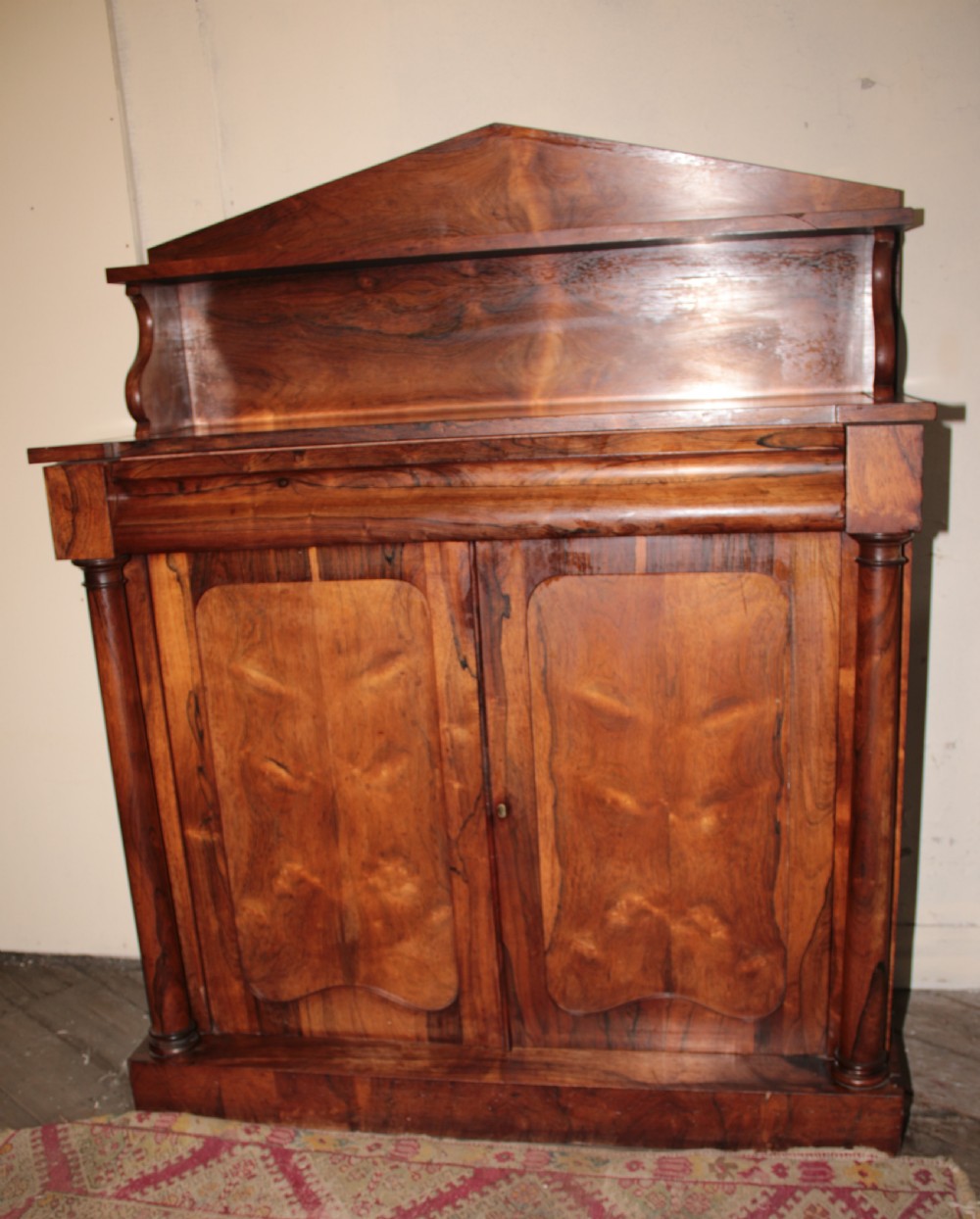 A Victorian rosewood chiffonier featuring a raised top display shelf, flame veneer cupboard doors, and turned side columns on a solid plinth base. View V