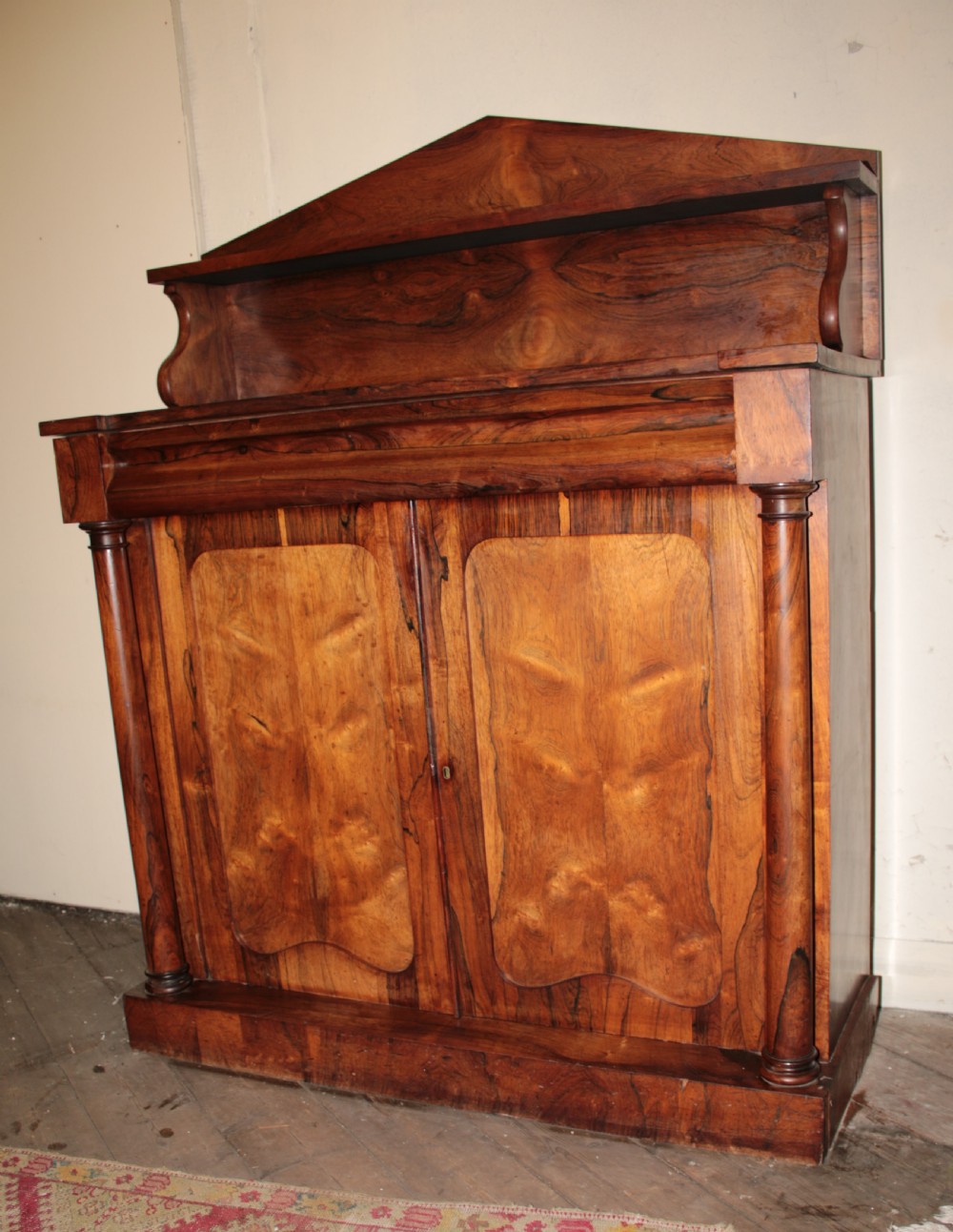 A Victorian rosewood chiffonier featuring a raised top display shelf, flame veneer cupboard doors, and turned side columns on a solid plinth base. View VI