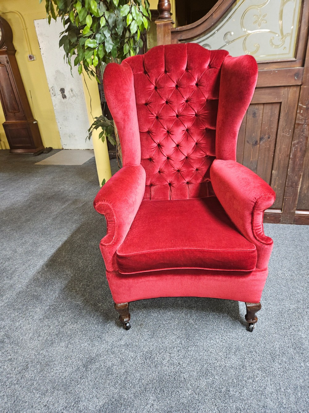A Victorian high-back wing chair upholstered in red velvet with diamond button tufting and turned timber front legs on castors.