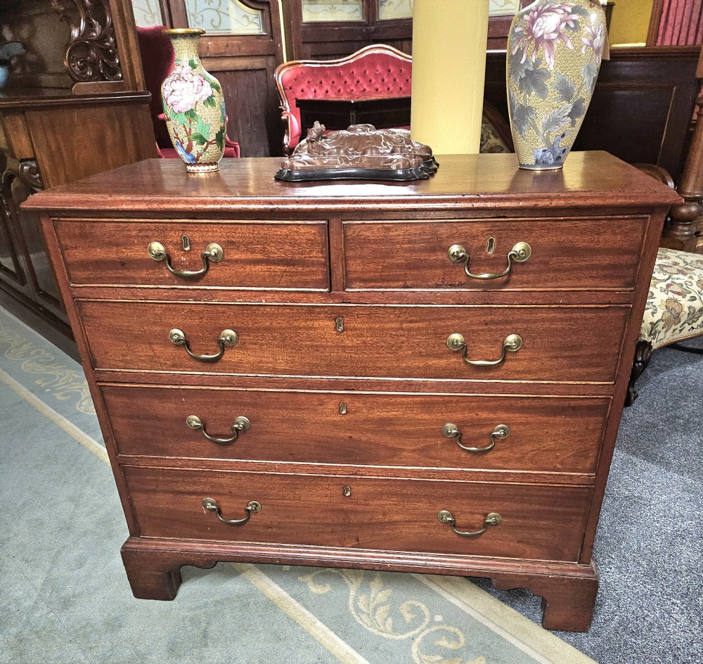 A rectangular Georgian mahogany chest of drawers featuring two short drawers over three long graduated drawers, fitted with brass swing handles and key escutcheons, raised on bracket feet. View II