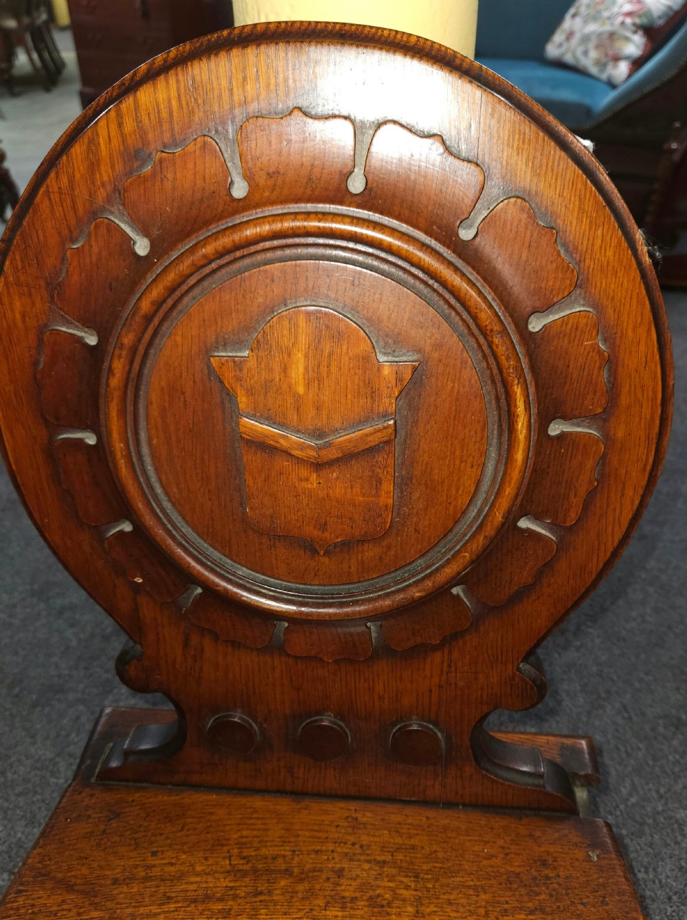 A Victorian oak hall chair featuring a rounded carved backrest with a central shield motif, a solid flat wooden seat, and turned front legs. View II