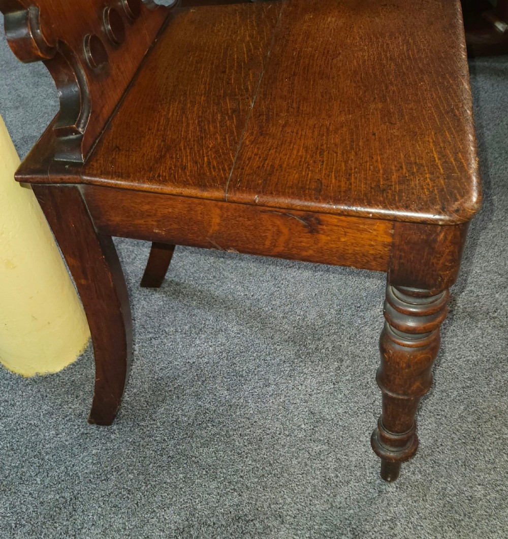 A Victorian oak hall chair featuring a rounded carved backrest with a central shield motif, a solid flat wooden seat, and turned front legs. View III