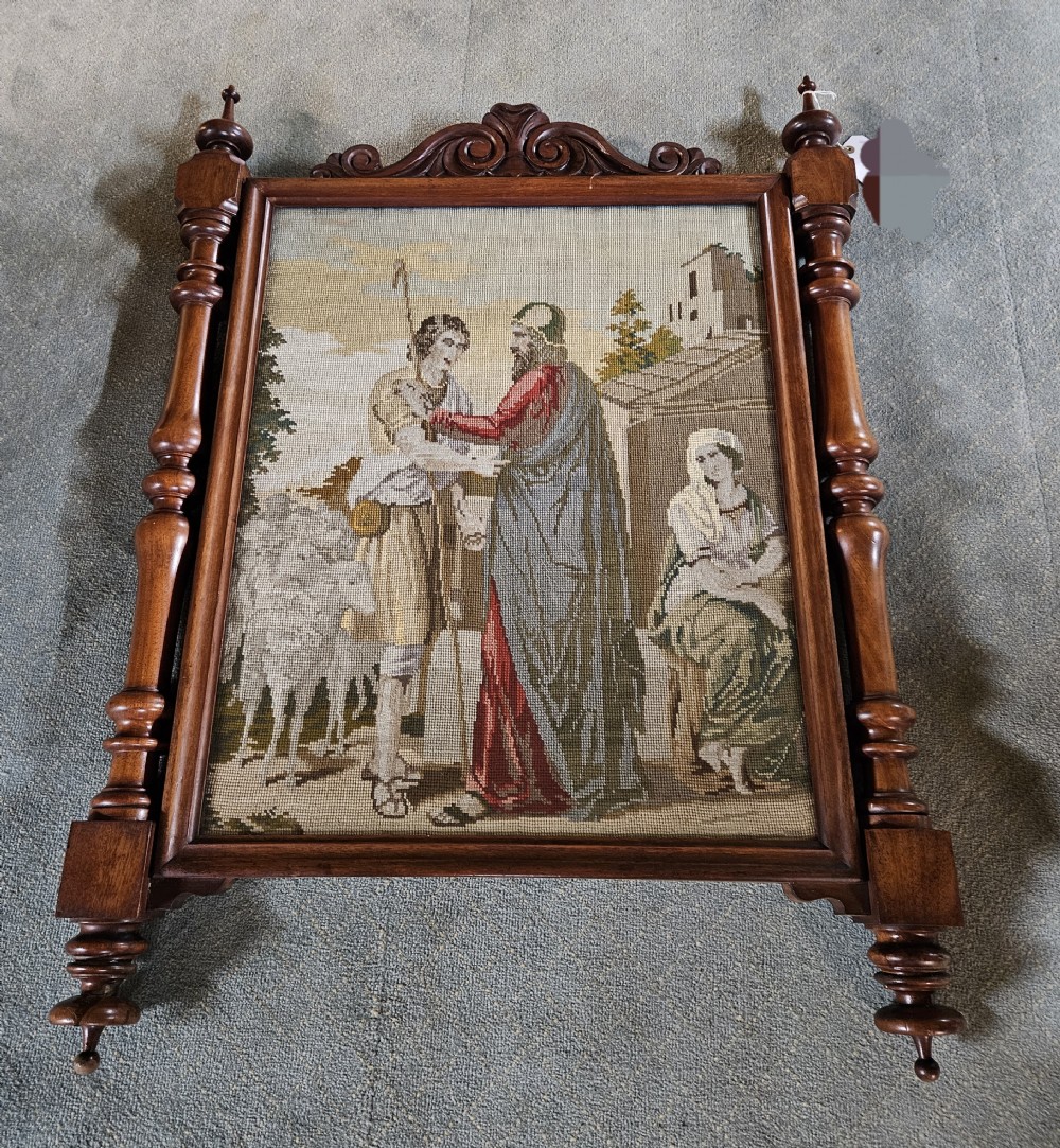 An antique Victorian needlepoint panel depicting a biblical scene enclosed in a carved mahogany frame with turned side spindles and finials.