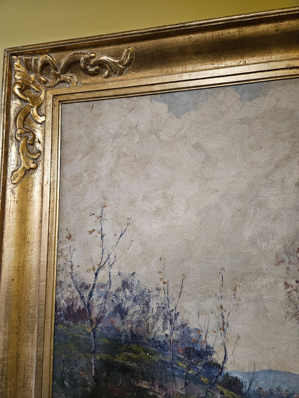 A large framed oil painting depicting a muddy countryside path lined with bare trees under an overcast sky, housed in an ornate gilt frame. View III