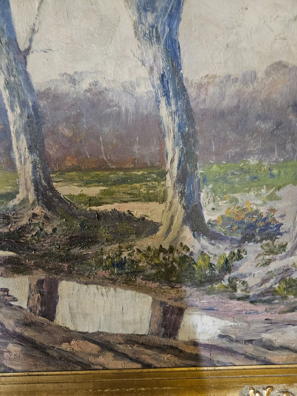 A large framed oil painting depicting a muddy countryside path lined with bare trees under an overcast sky, housed in an ornate gilt frame. View IX