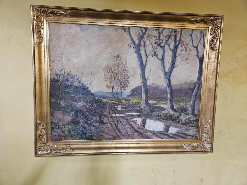 A large framed oil painting depicting a muddy countryside path lined with bare trees under an overcast sky, housed in an ornate gilt frame. View XI