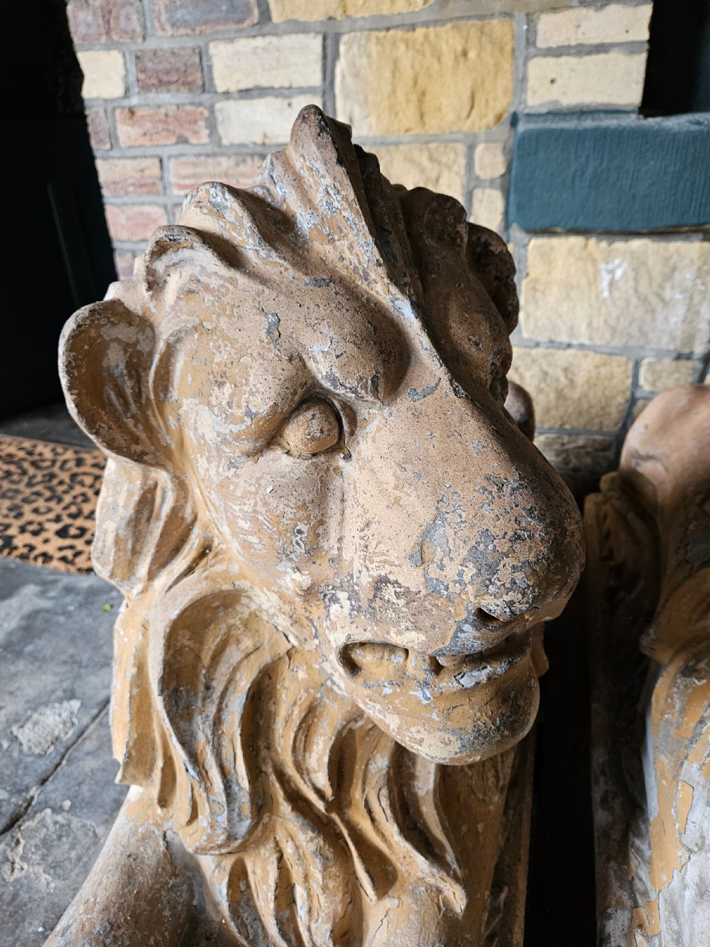 A pair of sculpted buff stone recumbent lion statues with detailed manes resting on integrated rectangular bases. View V