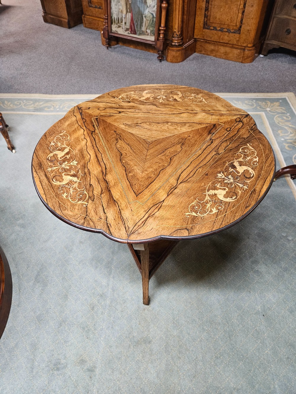 An inlaid rosewood drop-leaf table with extended circular scalloped leaves showing intricate floral marquetry and central geometric grain patterns.