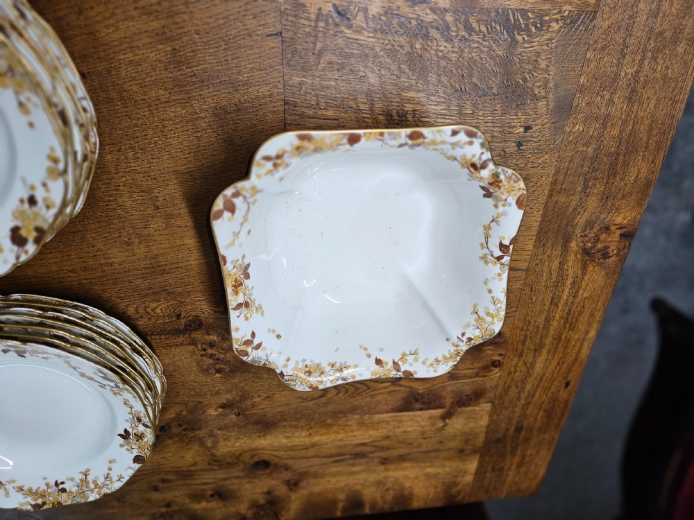 A white French porcelain dinner service with gold floral motifs displayed on an oak dresser and table. View II