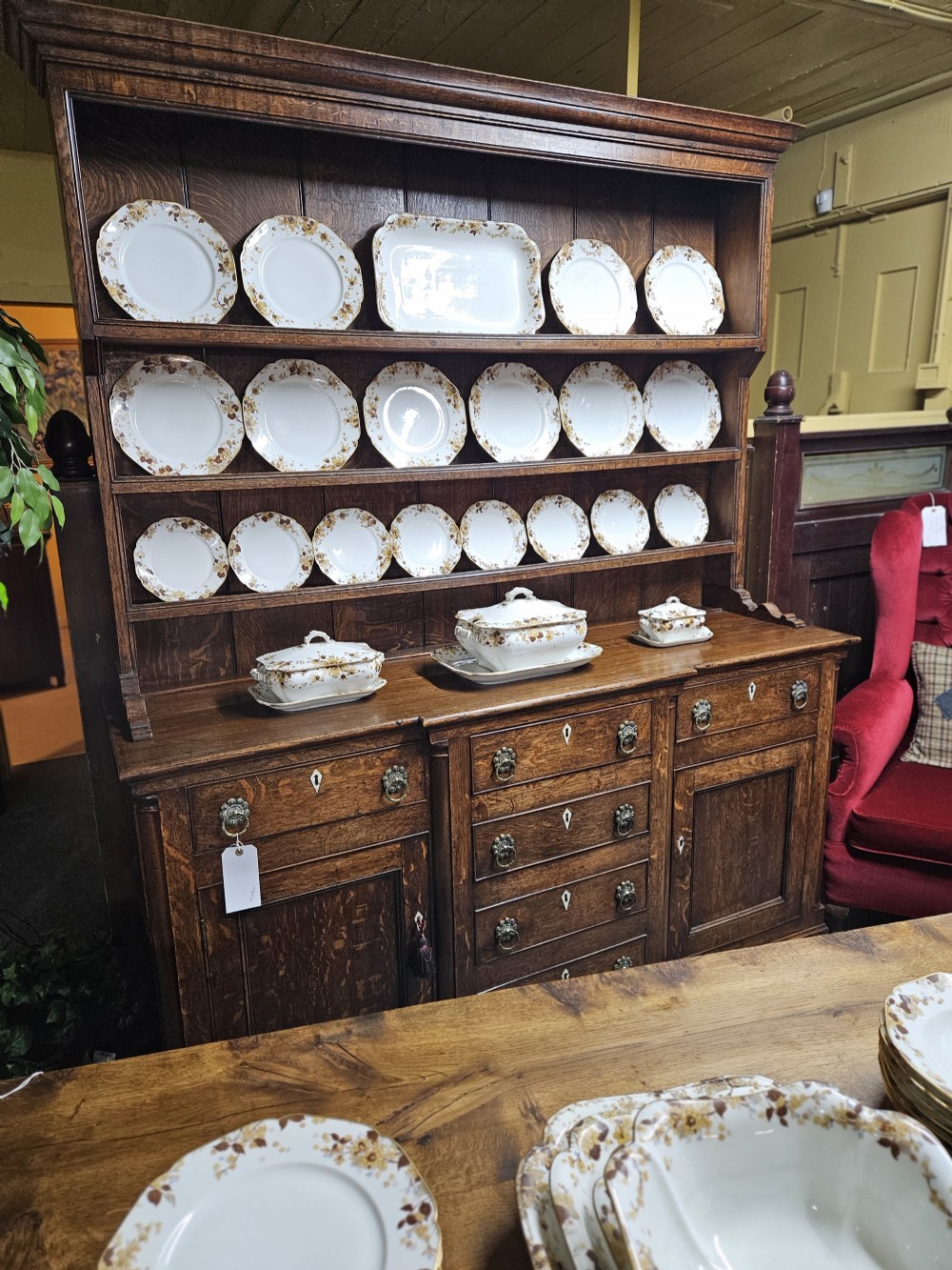 A white French porcelain dinner service with gold floral motifs displayed on an oak dresser and table.