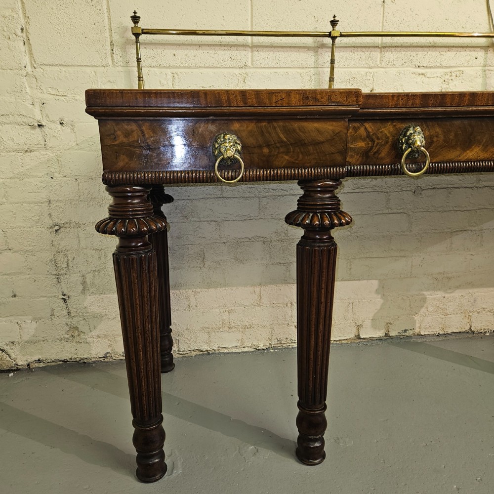 A Regency mahogany serving table featuring a brass gallery rail, lion mask ring handles, and six reeded tapered legs. View II