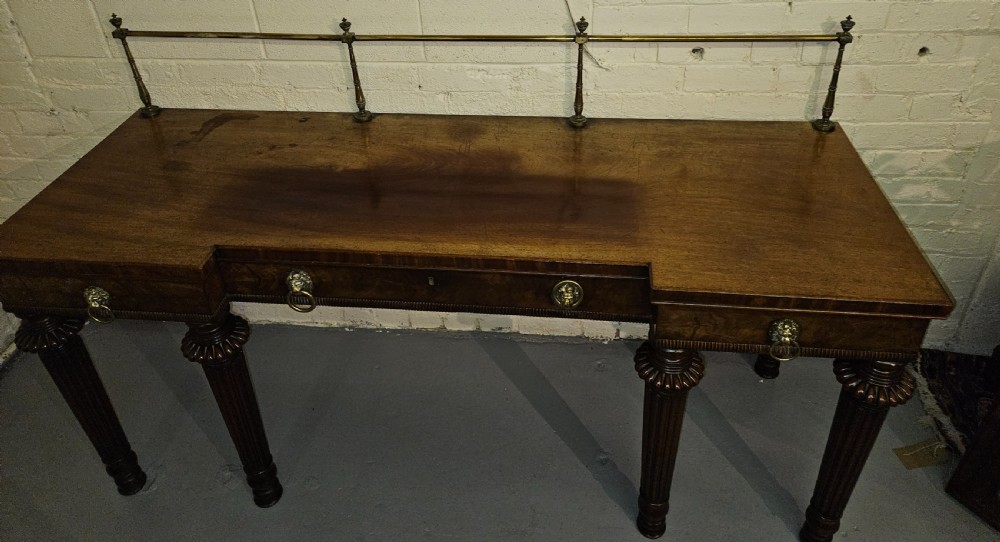 A Regency mahogany serving table featuring a brass gallery rail, lion mask ring handles, and six reeded tapered legs. View VI