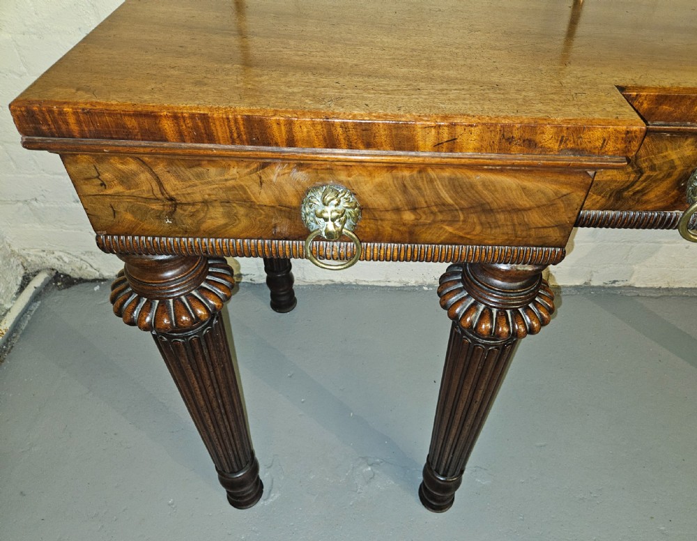 A Regency mahogany serving table featuring a brass gallery rail, lion mask ring handles, and six reeded tapered legs. View VIII