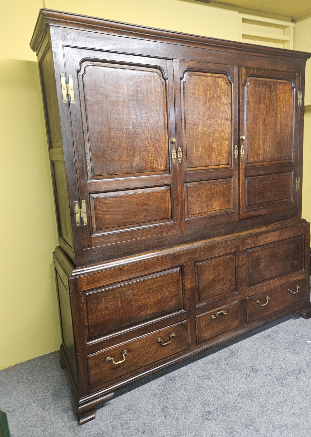A large period dark oak livery cupboard featuring fielded arch-topped panel doors above a lower section fitted with drawers and brass hardware. View II