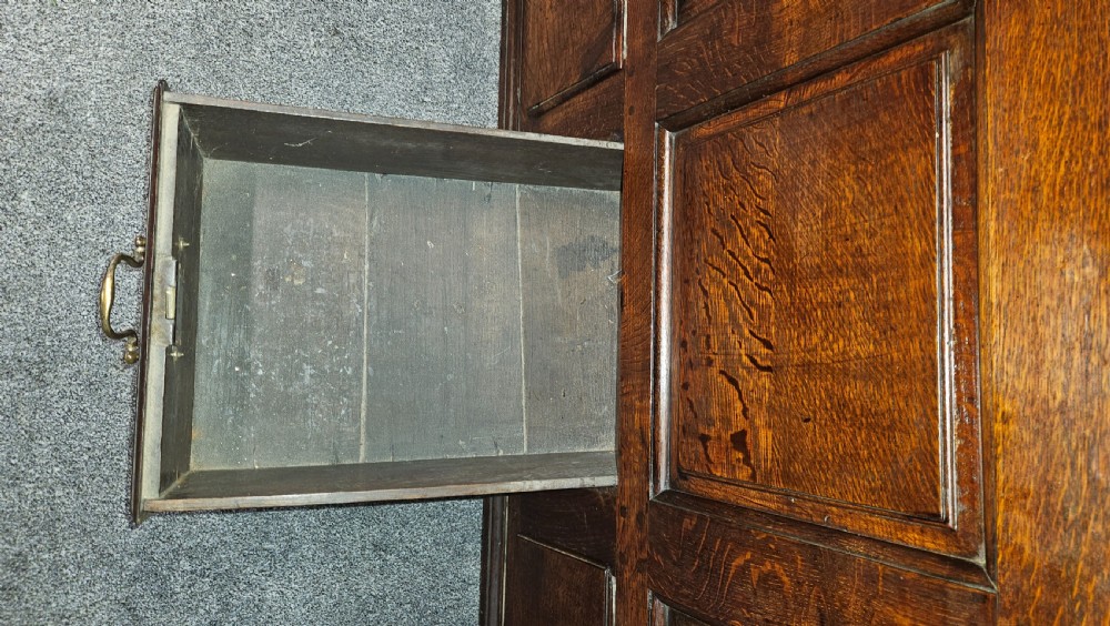 A large period dark oak livery cupboard featuring fielded arch-topped panel doors above a lower section fitted with drawers and brass hardware. View IV
