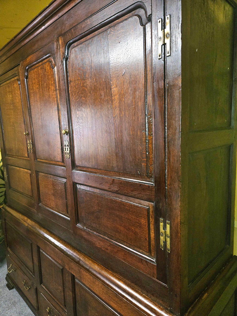A large period dark oak livery cupboard featuring fielded arch-topped panel doors above a lower section fitted with drawers and brass hardware. View VI