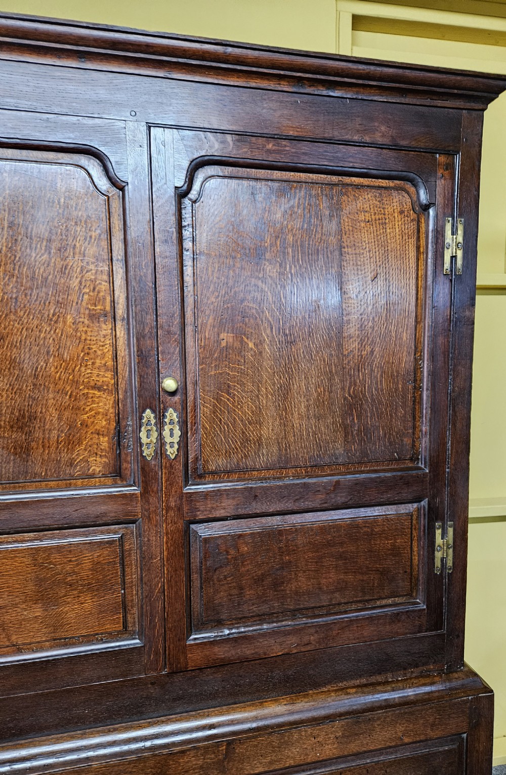 A large period dark oak livery cupboard featuring fielded arch-topped panel doors above a lower section fitted with drawers and brass hardware. View VIII